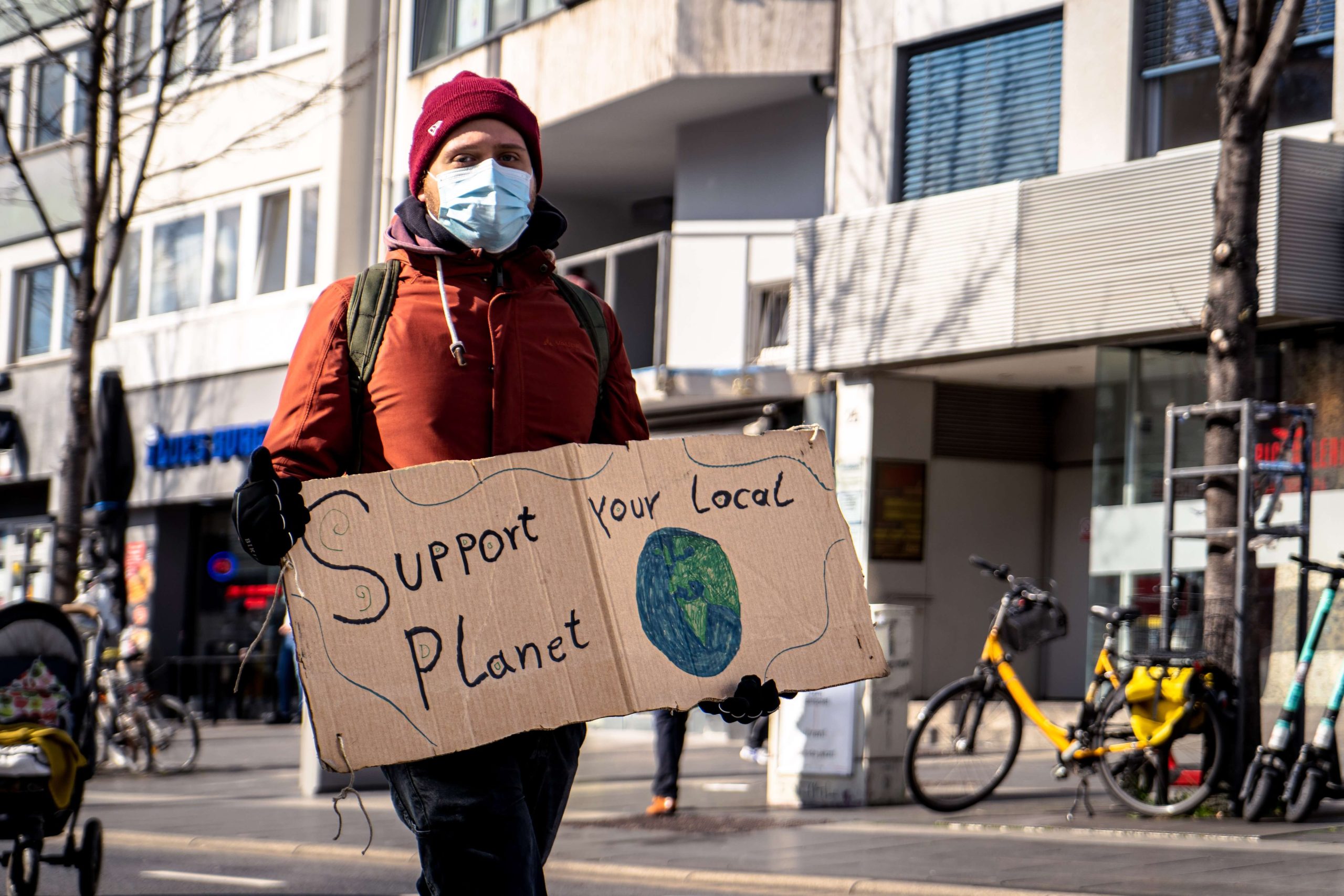 A person wearing a mask and holding a sign that says "support your local planet"