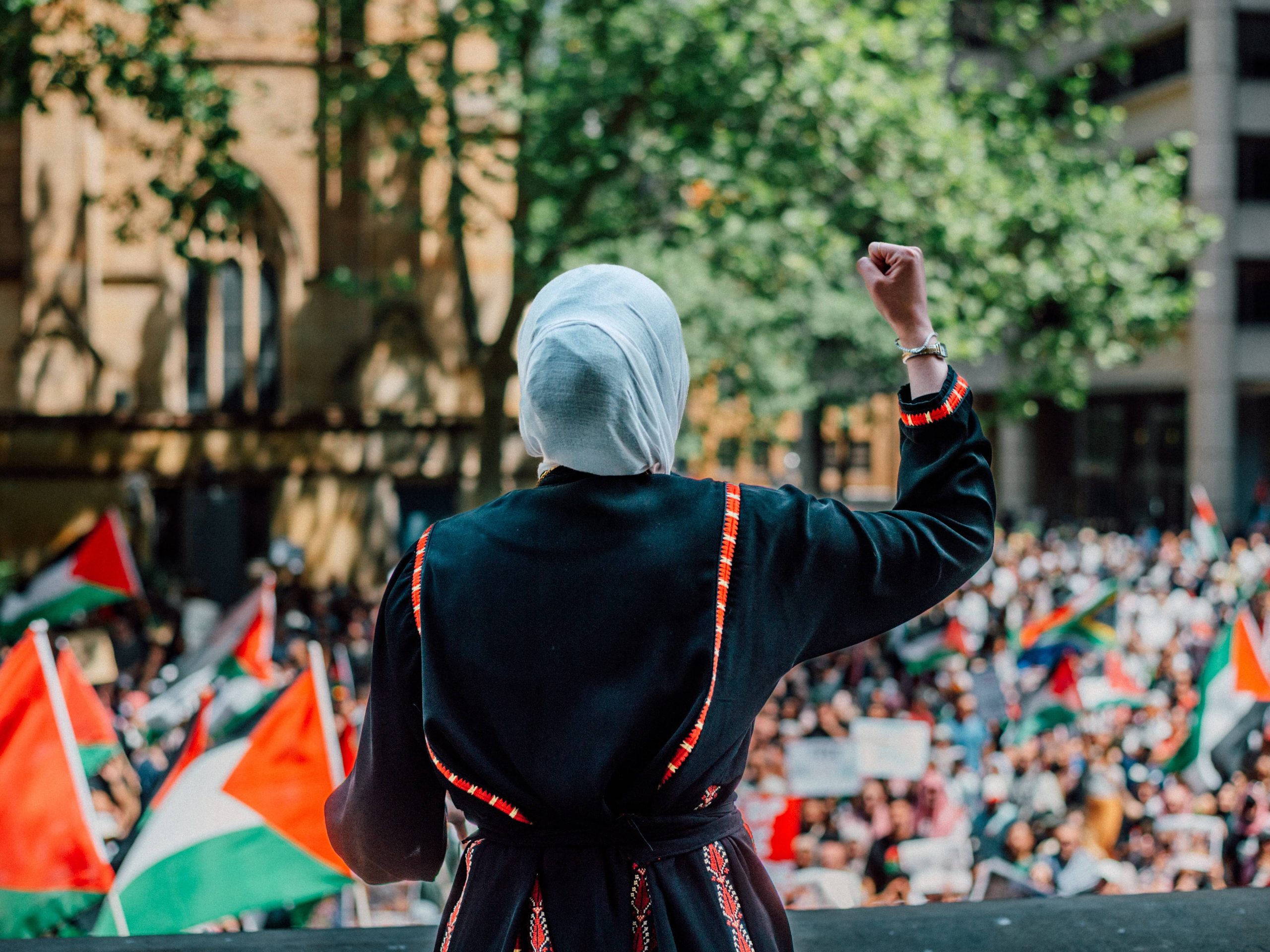 An image of a woman's back addressing a crowd at a pro-Palestine protest