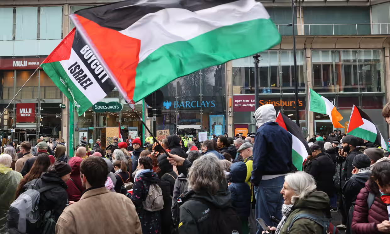 Image shows a number of protesters bearing the Palestine flag outside Barclays in London